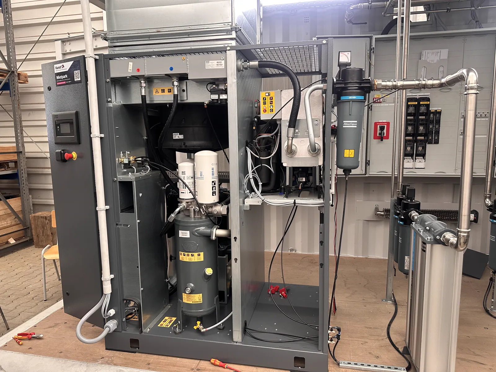 Kompressor mit geöffneten Verkleidungen während des Aufbaus, daneben Filter, Trockner und die Hauptverteilung des Containers