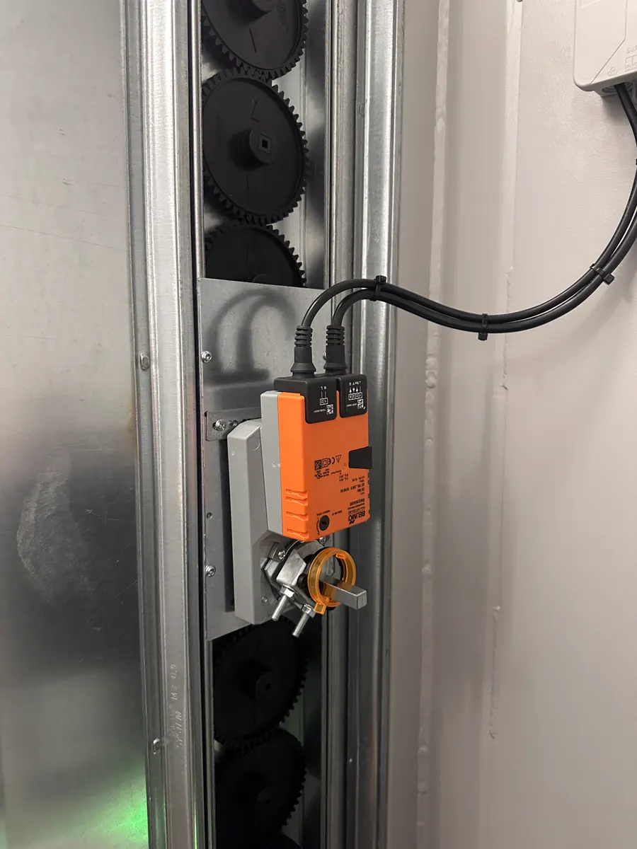 Orangefarbener elektrischer Stellantrieb an einer verzinkten Lüftungsklappe im Container