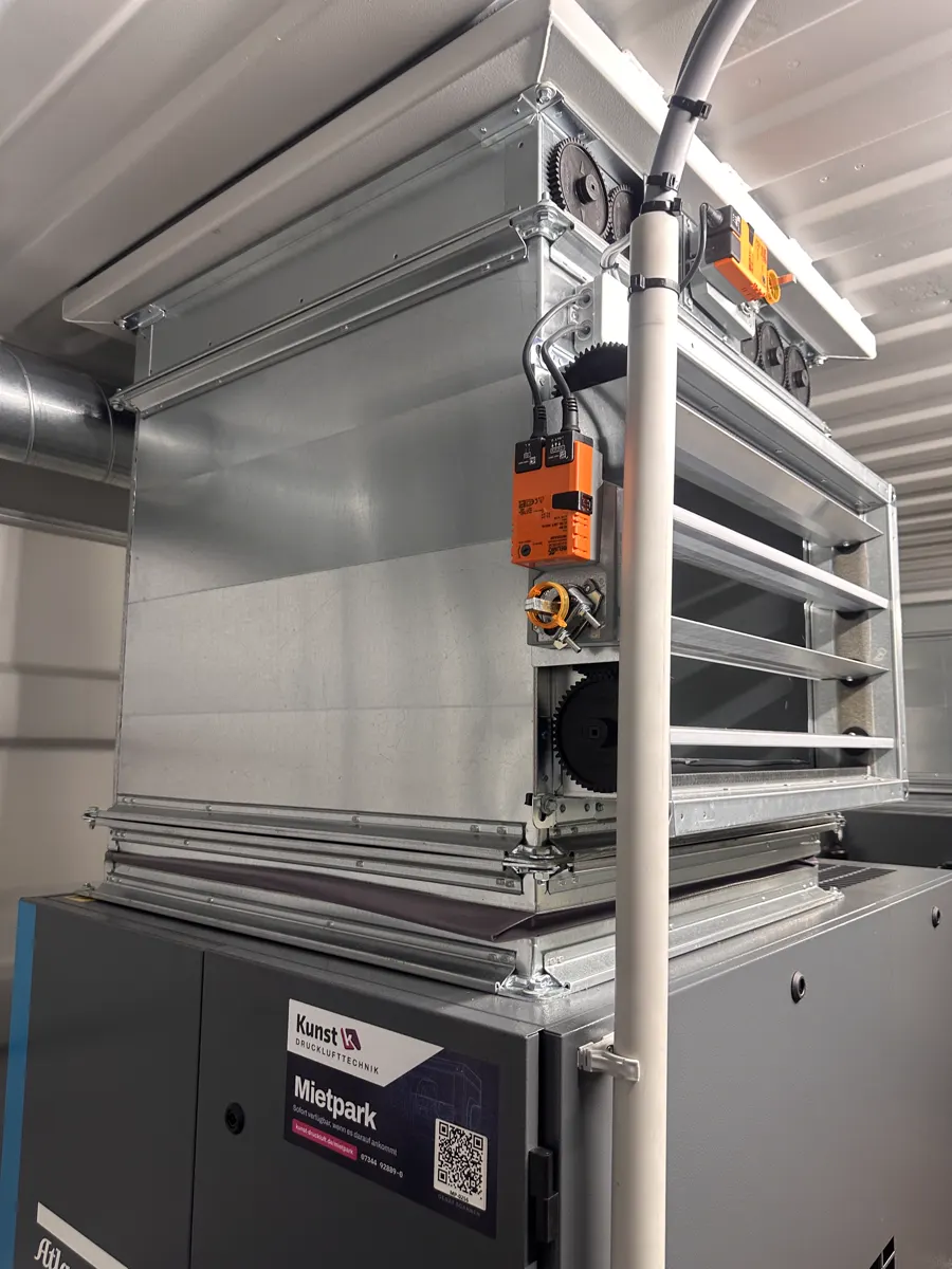Verzinkter Klappenkasten mit Lamellen und orangefarbenem Stellantrieb über einem Kompressor