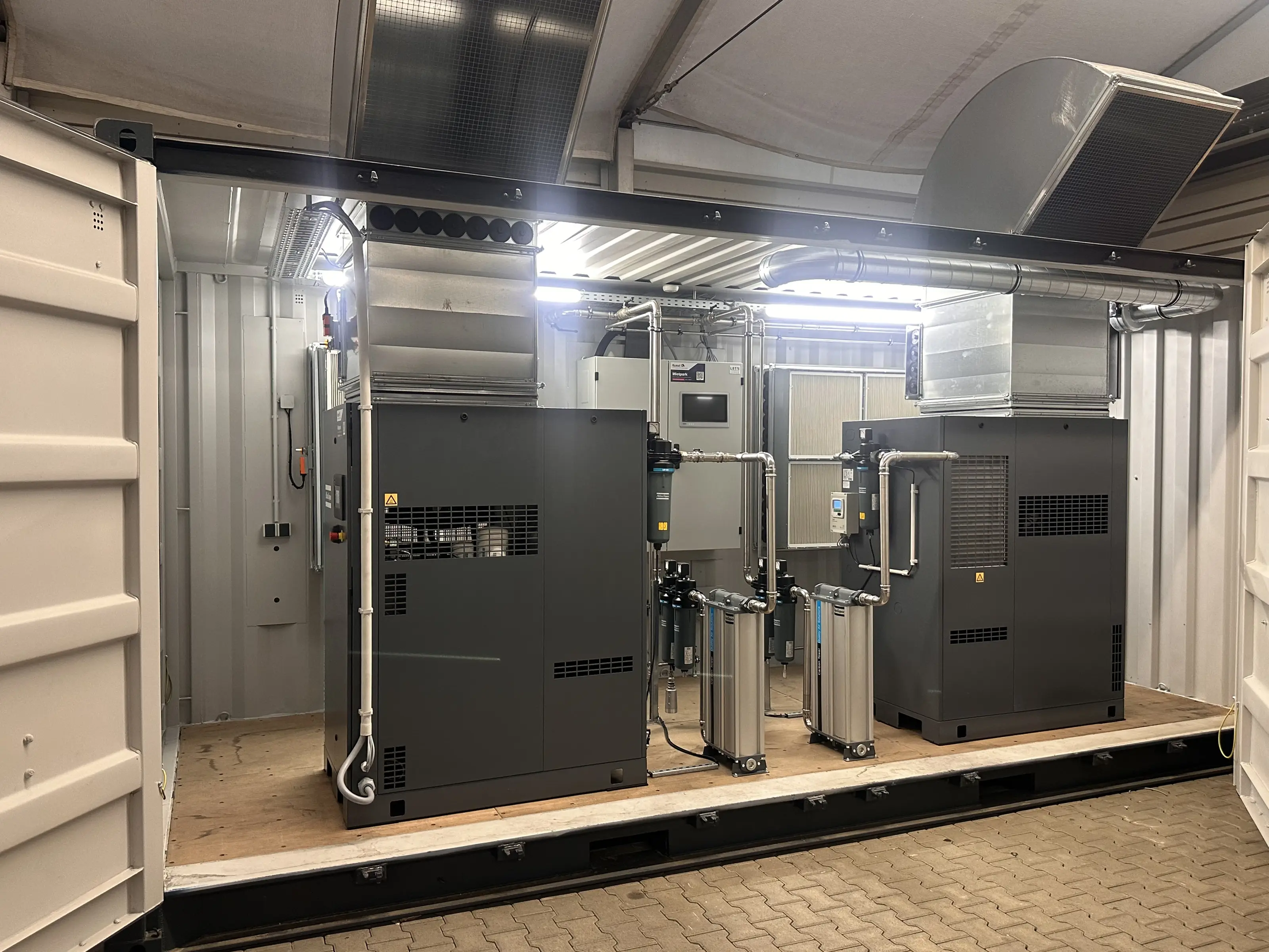 Geöffneter Kompressorcontainer von der Längsseite: zwei Schraubenkompressoren, dazwischen Filter und Aktivkohletürme, hinten Filterwand und Verteilung, oben Abluftkanäle